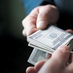 Close-up of hands exchanging a stack of dollar bills, symbolizing legal settlements, whistleblower claims, or financial compensation in legal cases